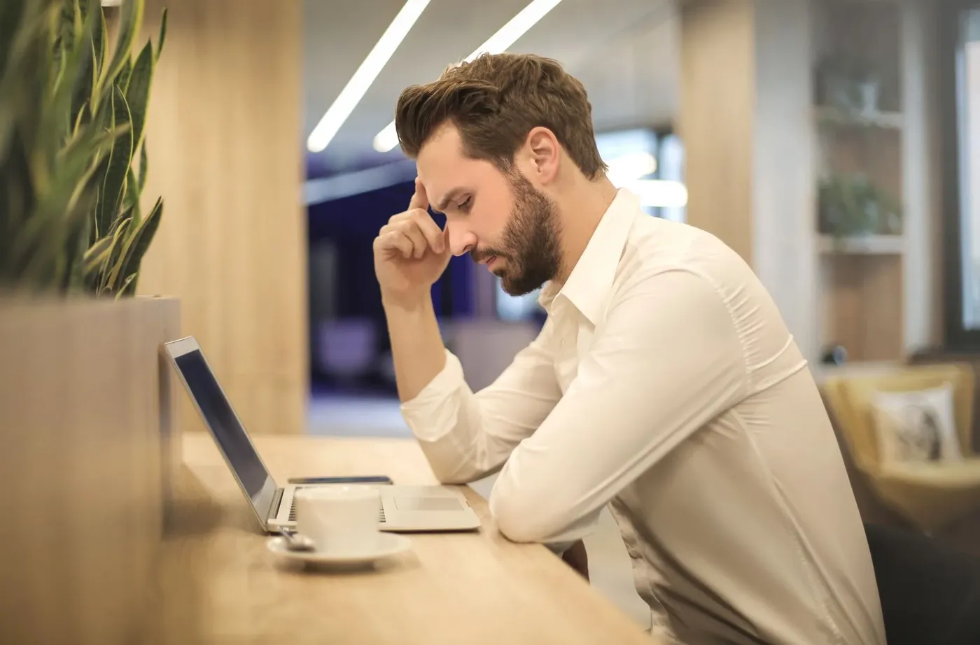 Man met hoofdpijn zit achter zijn laptop met zijn hand op zijn voorhoofd