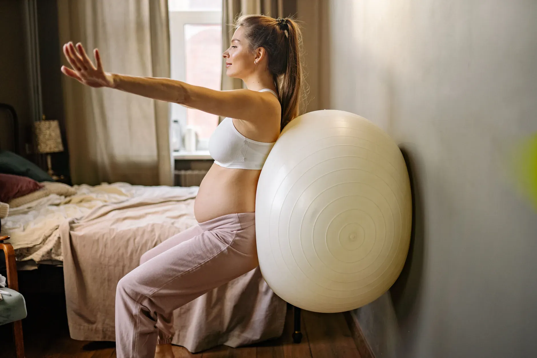 Zwangere vrouw doet een squat tegen een fitnessbal