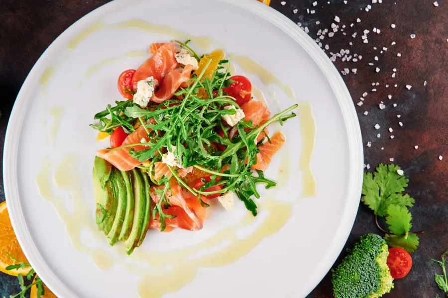 Bord met plakjes zalm, avocado, rucola en tomaat, besprenkeld met olijfolie