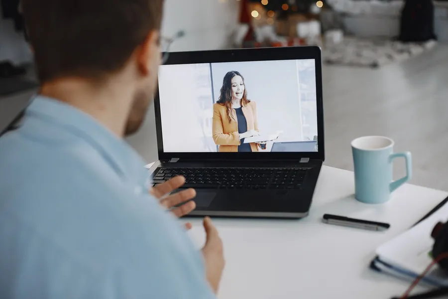 Man aan een bureau volgt op zijn laptop een online presentatie van een vrouw